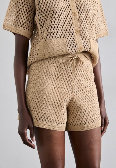 Tan knitted set featuring a short-sleeve, buttoned top and drawstring shorts. Both have a textured diamond pattern and ribbed edges.