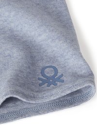 Světlomodrá pletená tkanina s jemnou texturou, na lemu s kruhovým logem v tmavší modré barvě a detailní prošitou hranou.