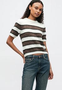 Gestreifter Pullover aus weichem, flauschigem Material. Abwechselnd dunkle braune und weiße Streifen mit kurzen Ärmeln und Rundhalsausschnitt. Trägt man mit Jeans.
