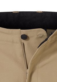 Beige Hosen mit einem Reißverschluss vorne und schwarzem Knopfverschluss, einer glatten Stoffoberfläche und einem Bund, der mit schwarzem Material gefüttert ist.