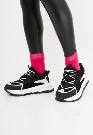 Zwart-witte sneakers met pluizige accenten, felle roze geribde sokken en een stevige textuurzool. Het ontwerp benadrukt comfort en stijl.
