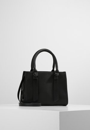 Schwarze Lederhandtasche mit doppelten Griffen und abnehmbarem Schulterriemen, die auf einer weißen Oberfläche vor einem einfarbigen hellen Hintergrund liegt.