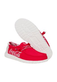Scarpe di tela rosse con suola bianca punteggiata, caratterizzate da un grande logo bianco della Coca-Cola e lacci, punta rotonda e lati testurizzati.