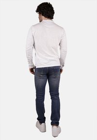 Camicia bianca a maniche lunghe con vestibilità comoda, abbinata a jeans blu in denim e sneakers bianche. La camicia ha un tessuto testurizzato.