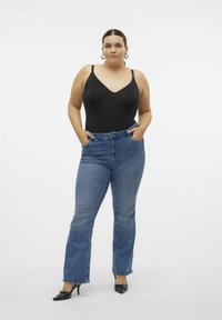 Black sleeveless bodysuit, dark blue flared jeans, and black heeled shoes. Smooth fabric, fitted design, and high waist with button closure.