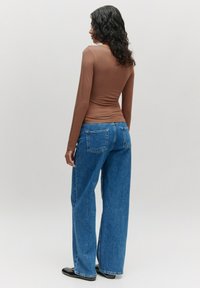 Braunes Langarmtop aus glattem Stoff, kombiniert mit hoch taillierten blauen weiten Denim-Jeans mit zwei Gesäßtaschen.