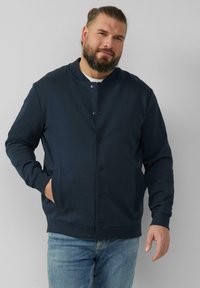 Marineblaue Sweatjacke mit Rundhalsausschnitt, featuring einer Druckknopfleiste, gerippten Bündchen und zwei seitlichen Taschen. Weiches Material.