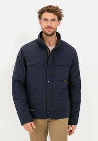 Navy gesteppte Jacke mit Stehkragen, zwei Brusttaschen und Knopfverschlüssen. Mit braunen Akzenten und einer strukturierten Oberfläche.