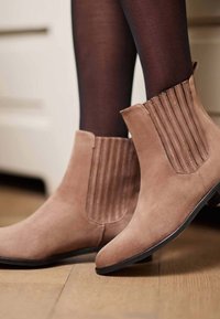 Bottines en daim tan avec des panneaux latéraux élastiques et un cône texturé. Présente une pointe arrondie et un petit talon carré sur une semelle noire.