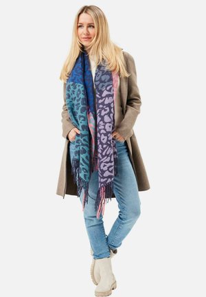 Woven scarf featuring a gradient of blue, purple, and pink with a leopard print pattern and fringed edges, styled with a beige coat and jeans.