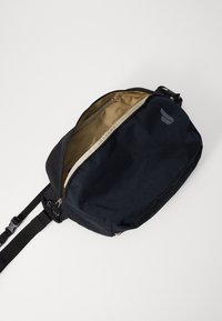 Black fabric shoulder bag with a smooth texture, zip closure, and an inner tan lining. Features an adjustable shoulder strap and logo detail.