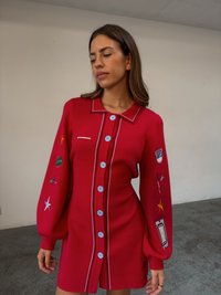 Czerwona dzianinowa sukienka z kołnierzem, niebieskimi guzikami i haftowanymi naszywkami na rękawach. Charakteryzuje się bufiastymi rękawami i dekoracyjnym ściegiem.