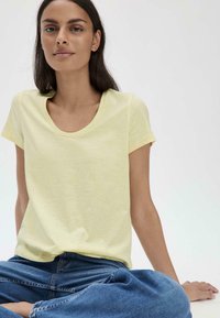 Gelbes Rundhals-T-Shirt mit kurzen Ärmeln, aus leichtem Stoff gefertigt, kombiniert mit blauen Jeans, bietet einen lässigen Schnitt und eine glatte Textur.