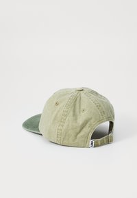 Khaki cap with a darker green visor, made of soft fabric. Features a circular top button and an adjustable strap at the back.