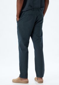 Mörkblå randiga byxor för män med elastisk midja, sidofickor, smal fotdesign och en texturerad yta.