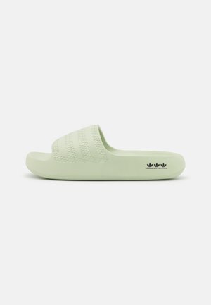 Jasnozielona klapka z trójwymiarowymi trzema paskami na pasku i małym czarnym logo Adidas po boku podeszwy.