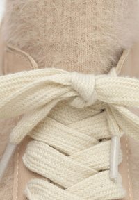Sneaker beige con tomaia testurizzata, dotata di un laccio intrecciato di colore crema. Aglet in metallo e dettagli morbidi e pelosi nella parte superiore.