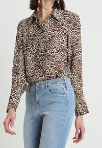 Bluse i leopardmønster med krave, lange ærmer og knaplukning, lavet af blødt stof. Sammen med lyseblå tætsiddende jeans.