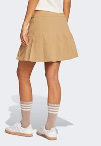 Tan pleated skirt with a smooth texture, featuring a mid-rise waistband. Paired with white sneakers and tan striped socks.