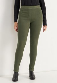 Olijfgroene legging gemaakt van rekbaar materiaal, met een hoge tailleband en een gladde textuur, gecombineerd met zwarte enkellaarsjes.