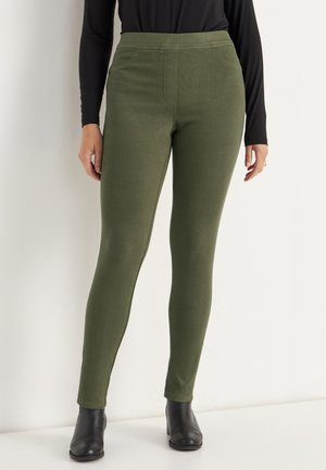 Olivenfarvede leggings lavet af strækbart materiale, med en høj talje og glat tekstur, parret med sorte ankelstøvler.