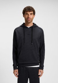 Felpa nera con motivo geometrico, cappuccio regolabile con coulisse e tasca a marsupio frontale. Tessuto morbido e texture; abbinata a pantaloni coordinati.