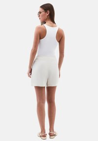 Top blanco sin mangas combinado con pantalones cortos crema. La tela es suave, con un ajuste relajado. Las sandalias tienen un diseño de tiras; las gafas de sol tienen un marco estampado.