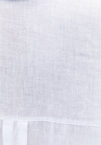 Primer plano de tela de lino blanca mostrando una textura de tejido fina y una costura cosida cerca del borde de la tela.