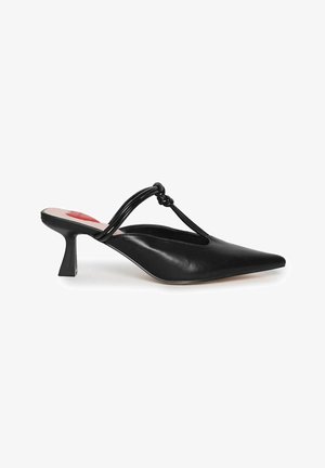 Black leather mules with a pointed toe, featuring a knotted strap and a small block heel. Smooth texture and sleek design.