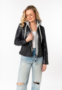 Zwarte leren jack met een grijze capuchon en trekkoorden, voorzien van een ritssluiting en verstoorde lichtblauwe jeans met gescheurde details.