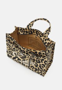 Laukku, jossa on leopardi-kuvio tan- ja mustassa kankaassa, missä on kaksi kahvaa, avoin yläosa ja sisäinen etiketti. Sisältää vetoketjullisen taskun ja tilavan pääosan.