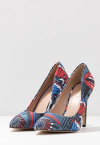 Des escarpins à talons aiguilles avec un imprimé de style bande dessinée aux couleurs bleu, rouge et noir, bout pointu et intérieur lisse beige.