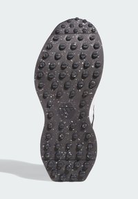 Black shoe sole featuring hexagonal and circular grip patterns, textured surface with small protrusions, and a central logo.