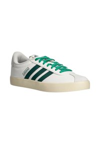 Zapatilla blanca de Adidas con rayas verdes y cordones verdes, suela beige y logo de Adidas en el lateral y la lengüeta, vista en ángulo.