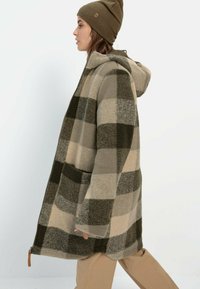 Kariertmantel in gedämpften Tönen von Beige und Olivgrün, mit Kapuze, lässiger Passform, Fronttaschen und Reißverschlussdetails am Saum.