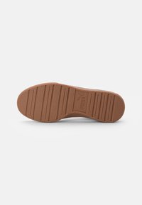 Suela de goma marrón de una zapatilla Puma con ranuras horizontales y el logo de Puma embossado en el centro, sobre un fondo blanco.