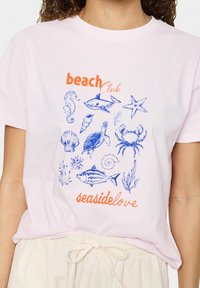 Svetle růžové bavlněné tričko s modrými ilustracemi na námořní téma a nápisem "beach Club" v oranžové barvě a "seasidelove" v oranžovém písmu.