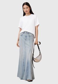 Gonna maxi in denim azzurro chiaro, aderente in vita, con orlo svasato e dettagli delle cuciture visibili. Abbinate a una t-shirt bianca a maniche corte.