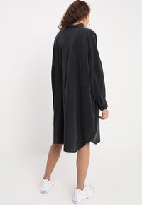 Schwarzes, übergroßes Hemdkleid mit langen Ärmeln, abgerundetem Saum und weichem Stoff. Verfügt über geknöpfte Manschetten und ein Yoke-Design auf der Rückseite.