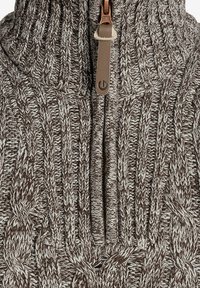 Brown and cream cable-knit pullover with a high collar, featuring a front zipper closure and leather pull tab for added detail.