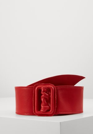 Large ceinture en cuir rouge avec une boucle rembourrée rectangulaire assortie reposant sur une surface blanche sur fond uni.