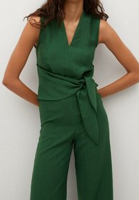 Combinaison sans manches en lin vert avec un col en V, taille nouée et coupe ample. Texture lisse et couleur unie sans motifs ni embellissements.