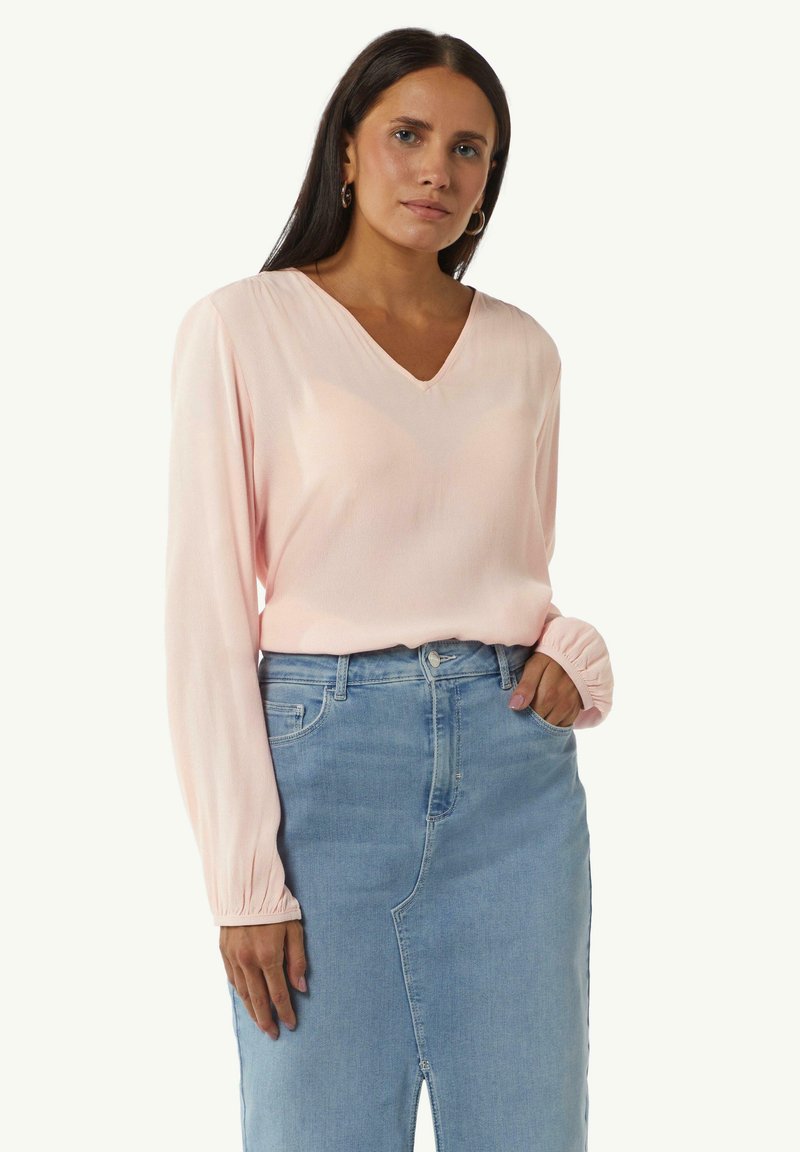 Rosa Langarmbluse mit V-Ausschnitt und gerafften Ärmelbündchen, kombiniert mit einem hellblauen Jeansrock mit seitlichem Schlitz.