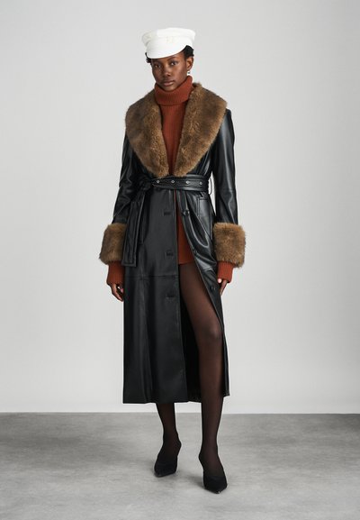 Melnas ādas trenča mēteli ar brūnu kažokādas apkakli un aprocēm, iepriekš sasietiem jostas vietā. Modelis valkā rūsu krāsas tūrti un melnās augstpapēžu kurpes.