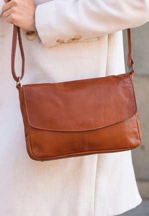 Hnědá kožená crossbody taška s klopou, plochým obdélníkovým tvarem a jedním popruhem, s hladkým, texturovaným povrchem.
