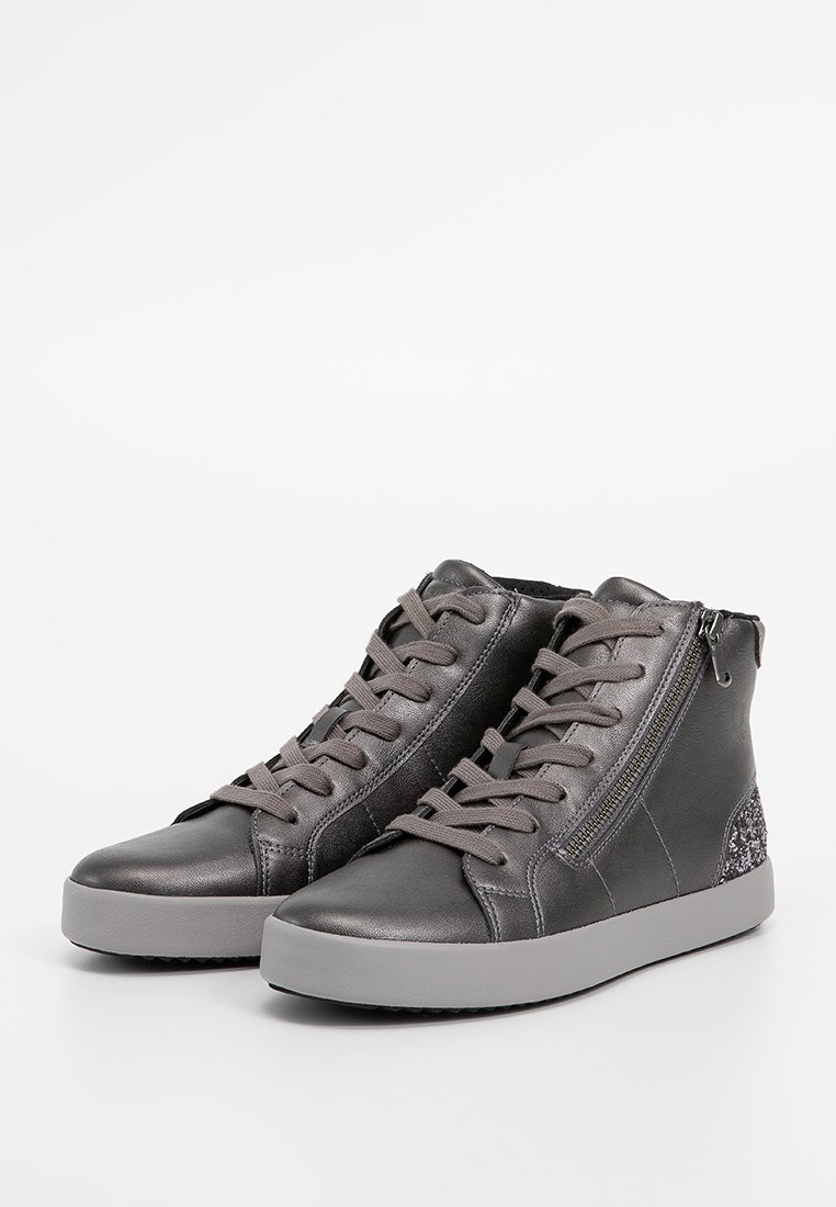Une paire de baskets montantes en cuir noir avec des zips sur le côté, des lacets gris et un détail texturé au niveau du talon sur des semelles en caoutchouc gris.