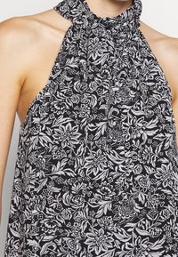 Top sin mangas de estampado floral en blanco y negro con escote fruncido y corte suelto. Presenta patrones intrincados de flores y hojas. Tejido ligero.
