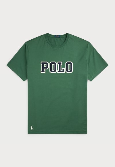 T-shirt de algodão verde com um grande logótipo "POLO" em branco e azul marinho. Mangas curtas, gola redonda e pequeno detalhe do logótipo na bainha.