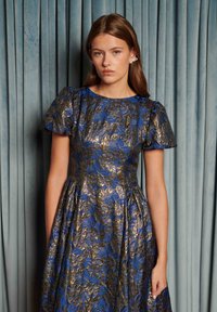 Modré a zlaté kvetinové šaty s krátkymi nadýchanými rukávmi, priliehavým živôtikom a rozšírenou sukňou; látka má textúrovaný vzor s leskom.