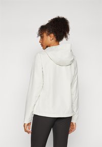 Vit huva jacket med en slät textur, justerbar dragsko och långa ärmar, bärs över svarta byxor. Bakåtsidan visar en avslappnad passform.
